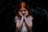 A moody photo of a pale young girl with red hair holding her head in her hands