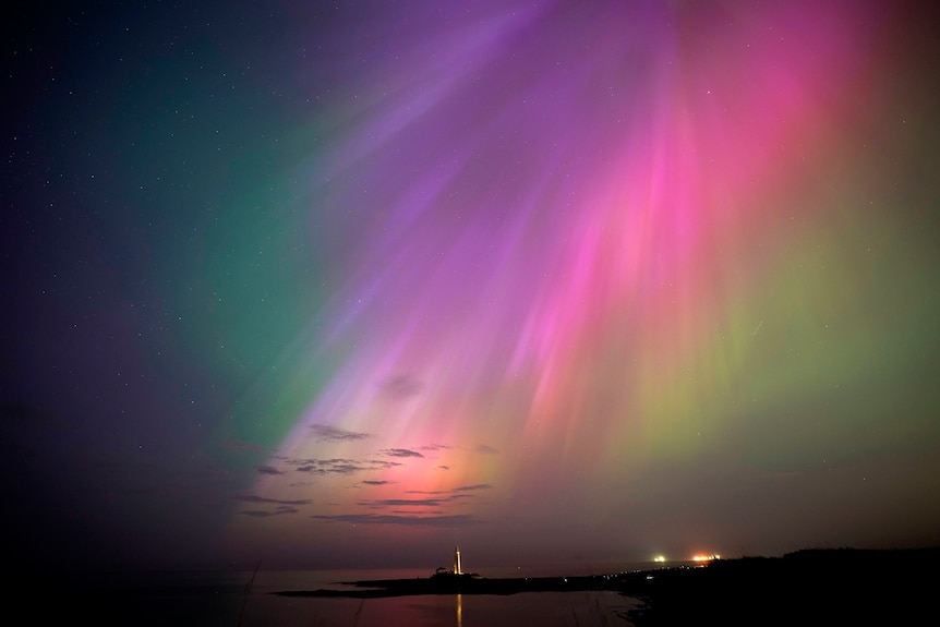 purple, green, yellow and pink hues of the Northern Lights above a lighthouse