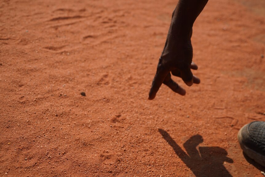 A hand points to tracks in red dirt