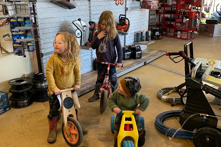 Three young children play on bikes in a farming supply store