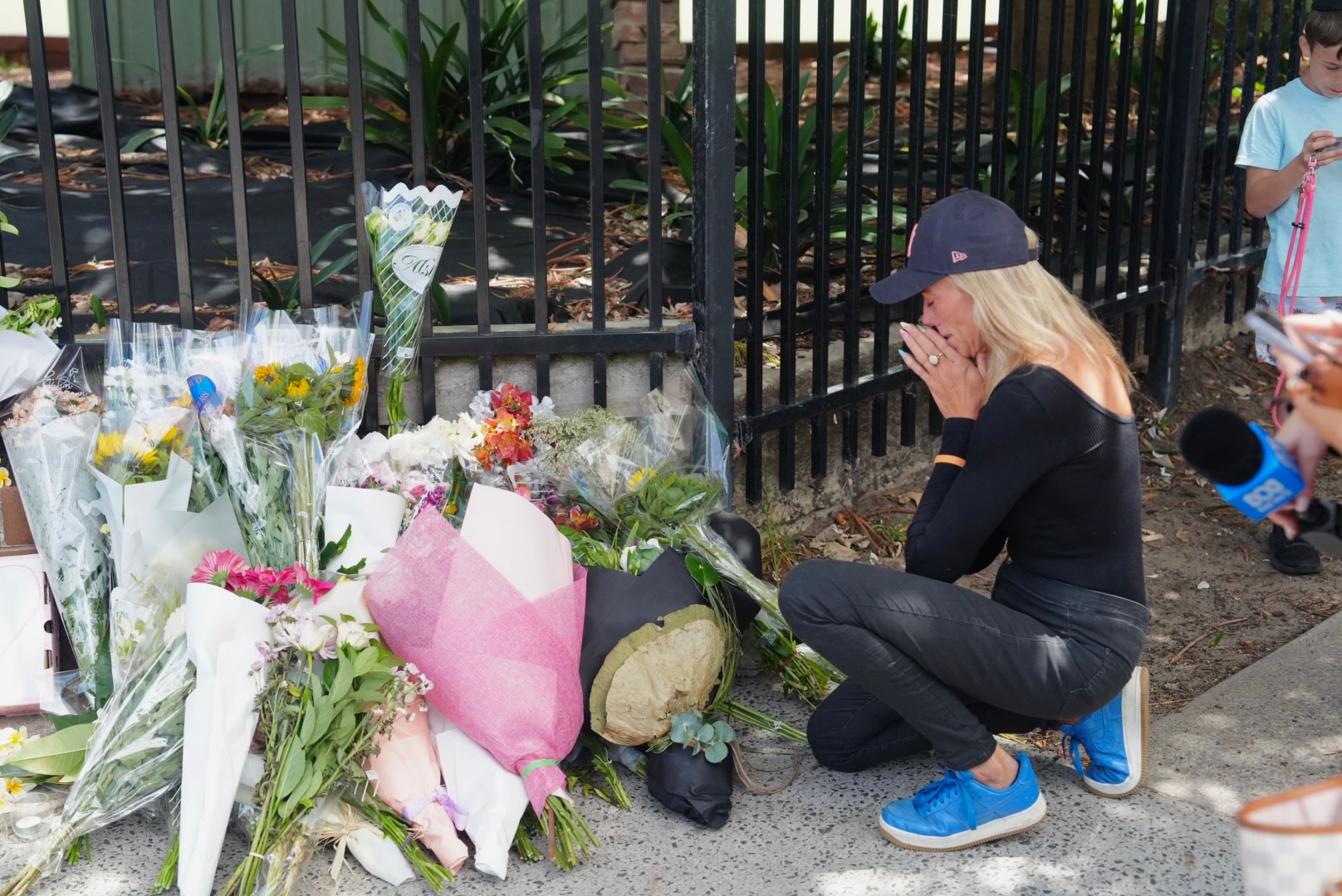 Uma mulher se ajoelha e reza diante de uma homenagem floral em Bondi Beach.