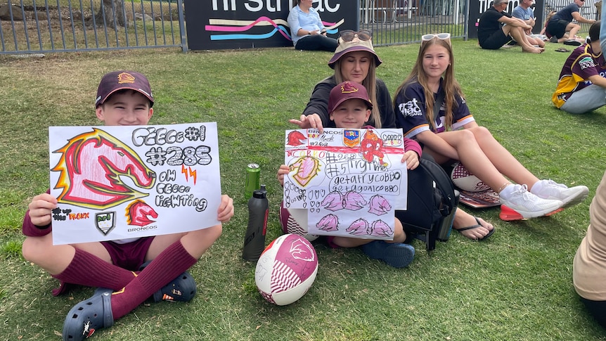 Two boys, a daughter and their mother hold hand-drawn Broncos and "reece lightning" signs on a grassy lawn.