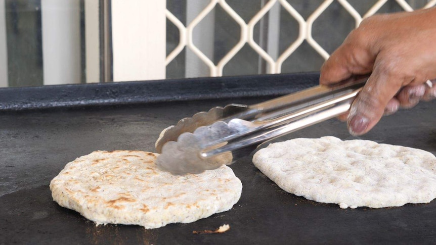 A person's hand flips flatbreads on a barbecue using tongs.