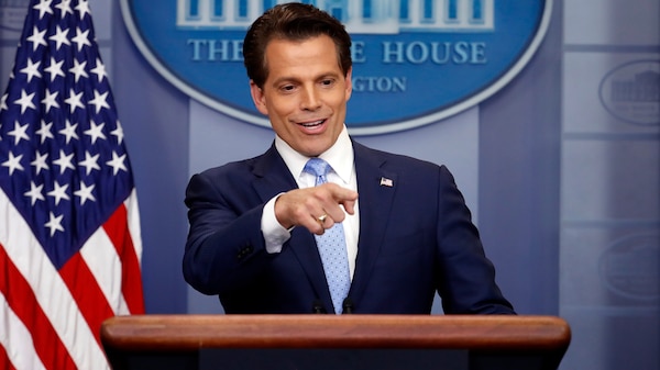 A man in a suit stands at a lectern with an American flag, pointing