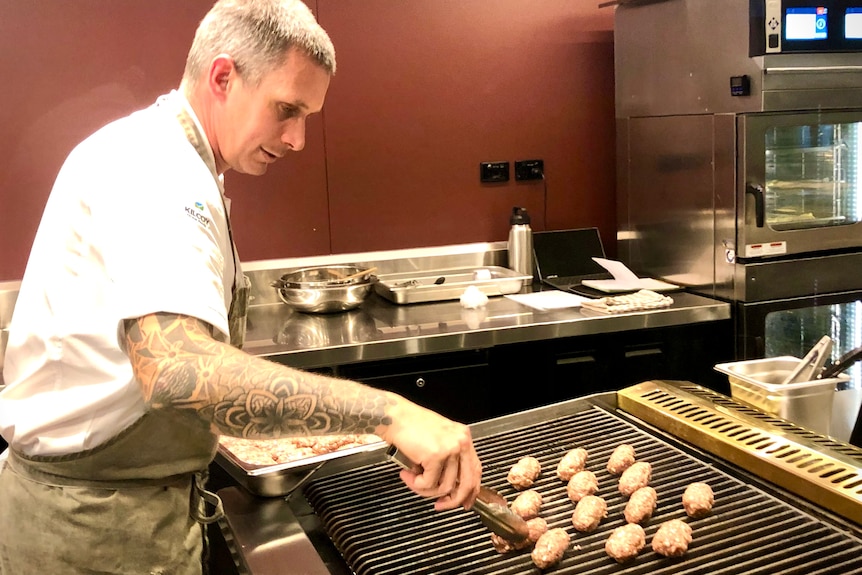 A chef with a tattooed arm, grills meat.