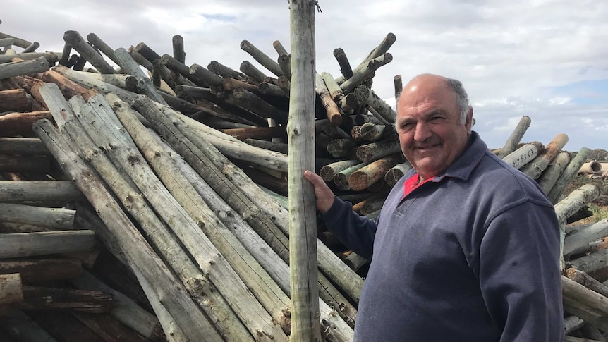 A man stands in front of a pile of old wooden posts.