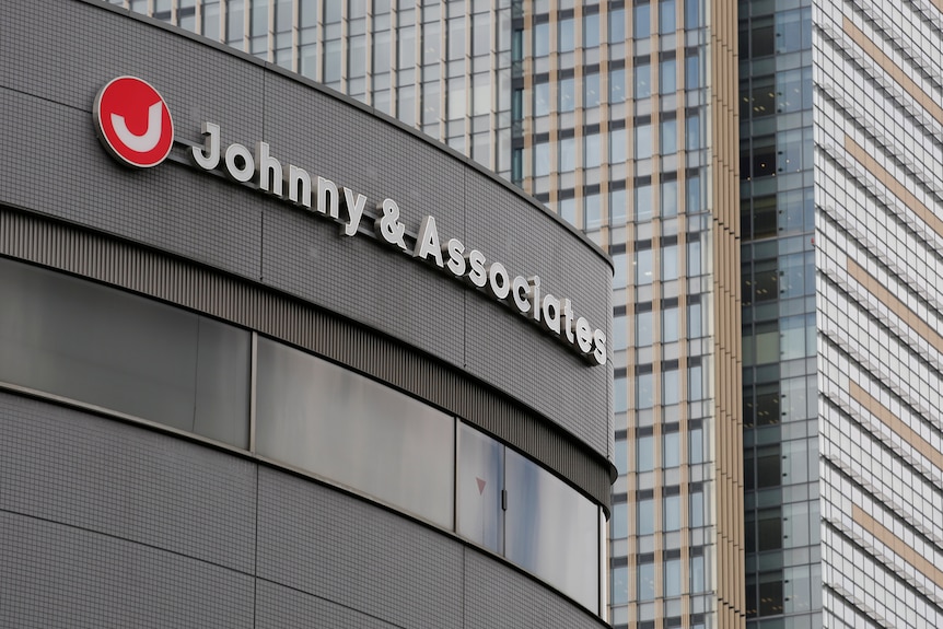 A sign with logo of a red circle with a white J and 'Johnny & Associates' sits atop an office building 