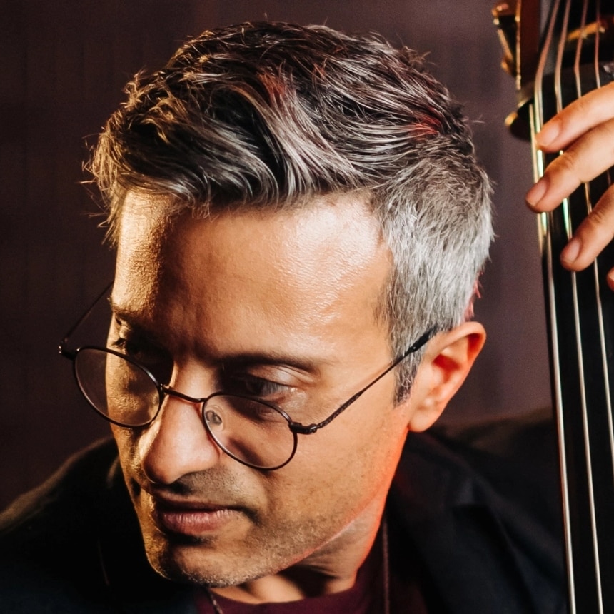A close-up photo of bassist Adam Ben Ezra with his double bass; he's wearing glasses and is looking to his left