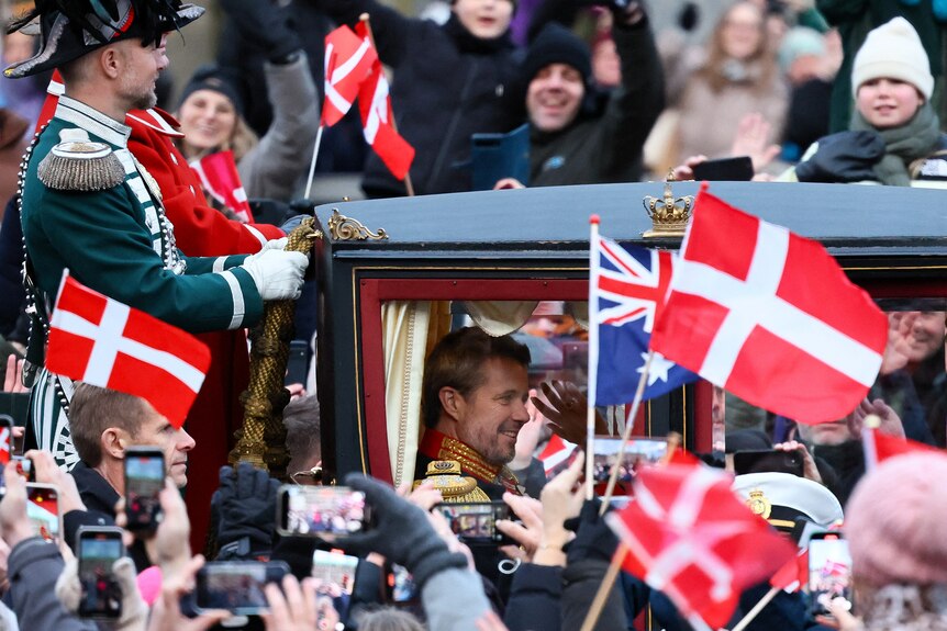 Frederik sits in a carriage swarmed by people holding up Danish and Australian flags.