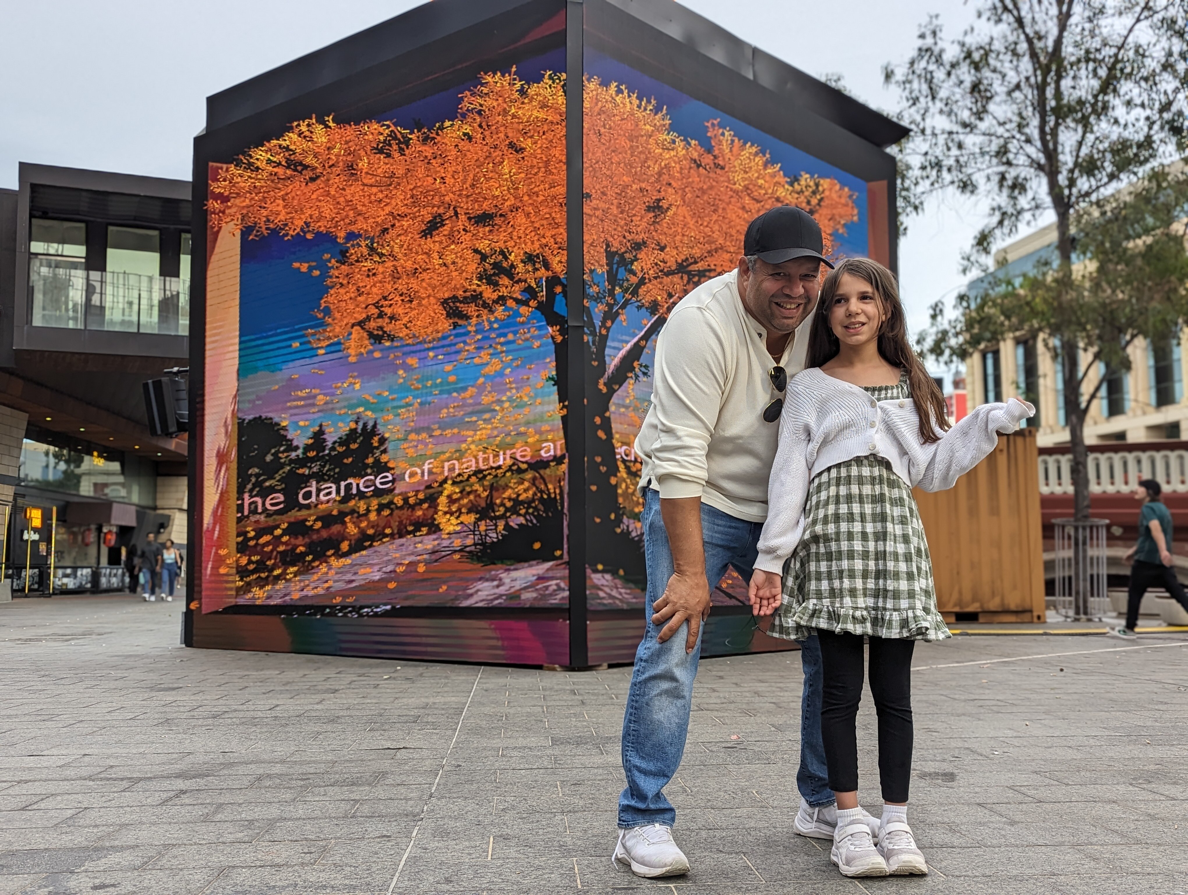 Phil Walleystack and his daughter Cara smiling and standing in front of the big screens for the video art installation.