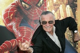A man wearing dark glasses adopts a Spider-Man pose in front of a Spider-Man poster
