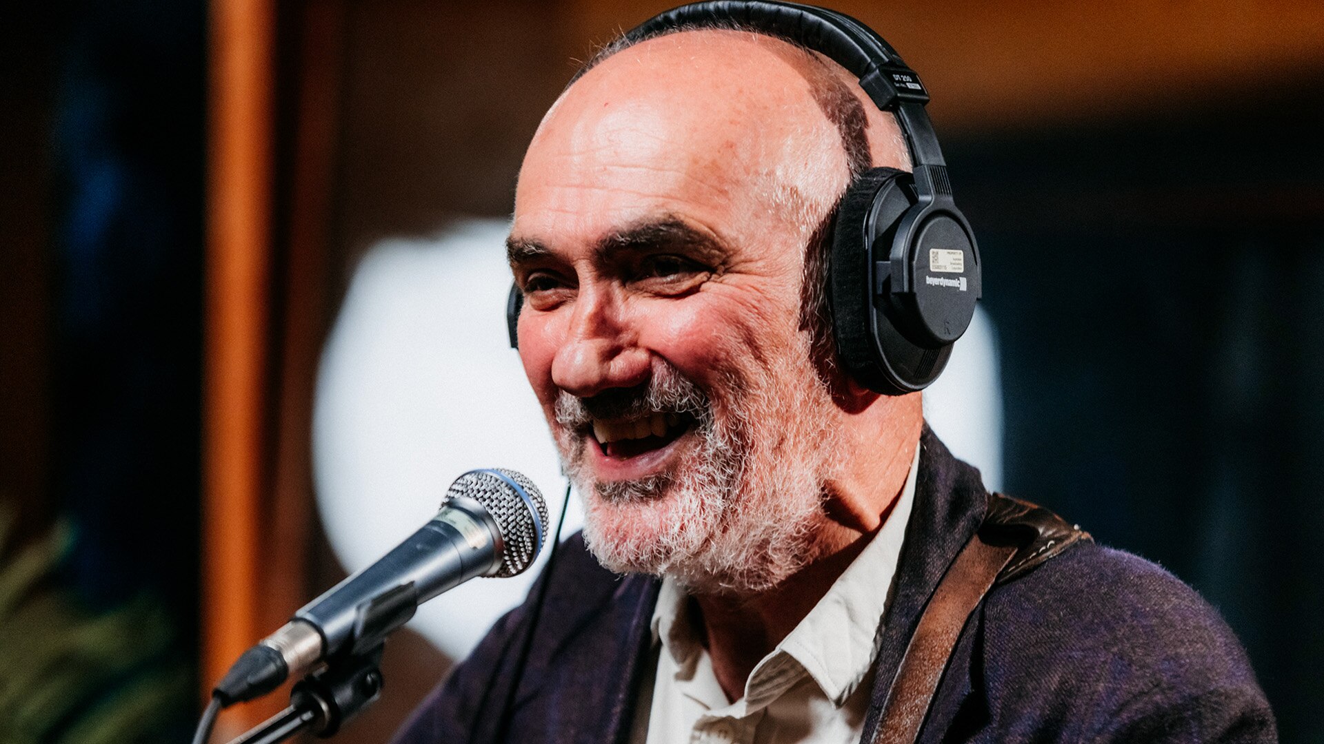 Paul Kelly, wearing headphones, smiles and sings into a microphone in studio performance