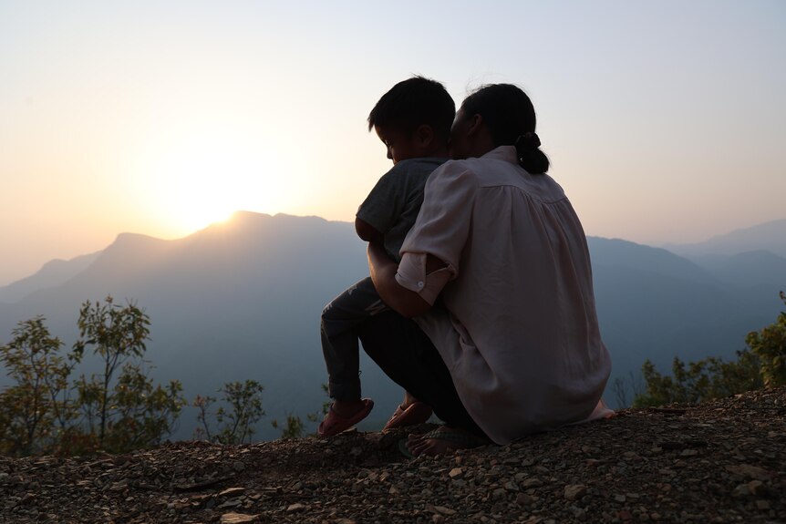 Mother and son sit in mountains watching sun set