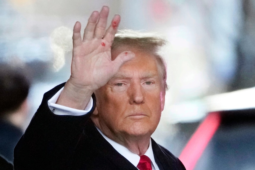 A stern looking Donald Trump waves as he walks onto city street