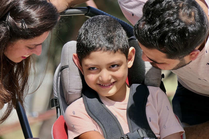 Young boy Kayaan is sitting in a chair with a huge smile, as both his parents smile at him.