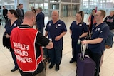 A group of nurses wearing navy scrubs stand in an airport