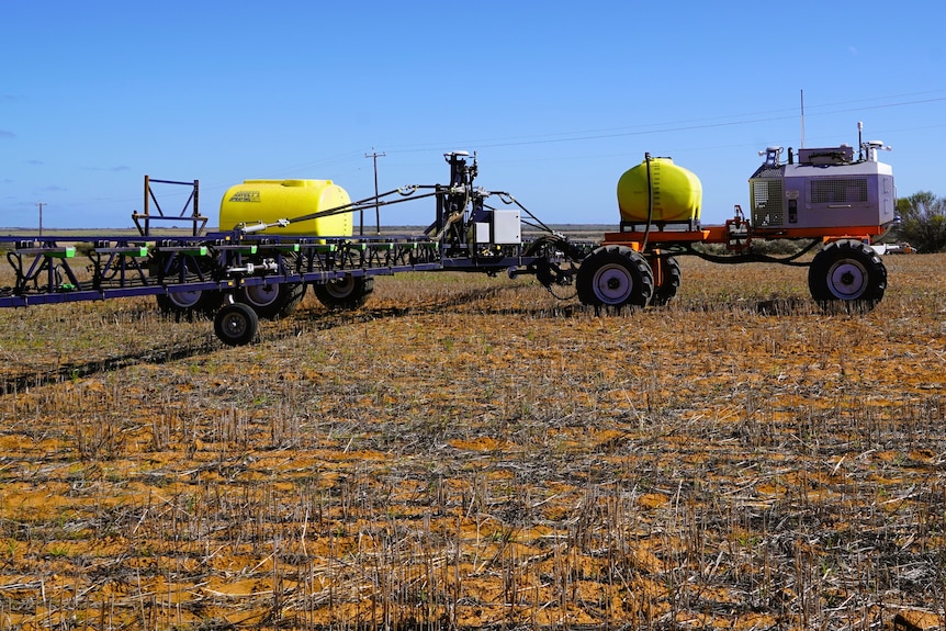 A side view of a robot crop spraying machine on land with brown stubble, blue skies.