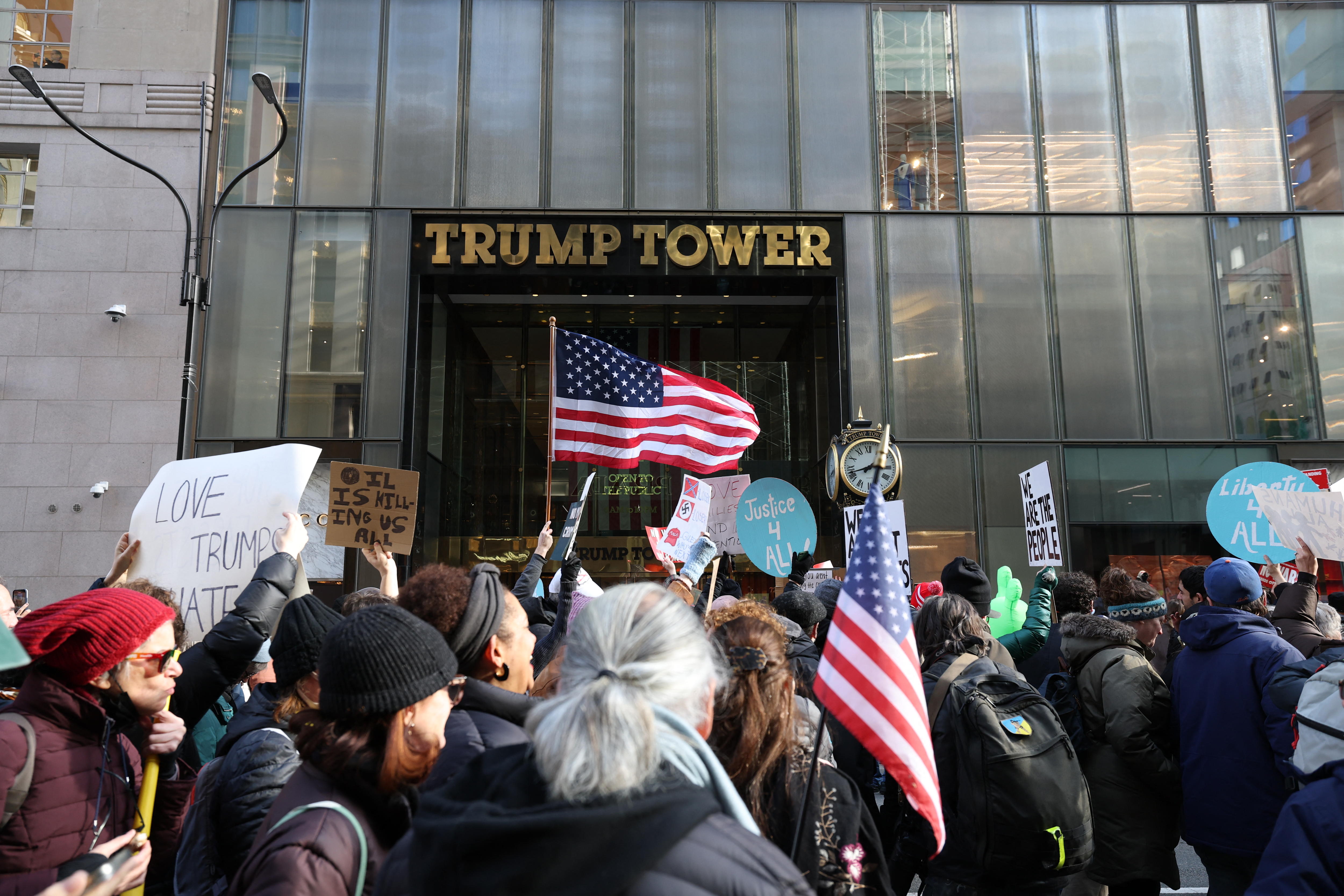 Decenas de manifestantes se encuentran frente a la entrada de la Torre Trump. Algunos sostienen banderas estadounidenses.