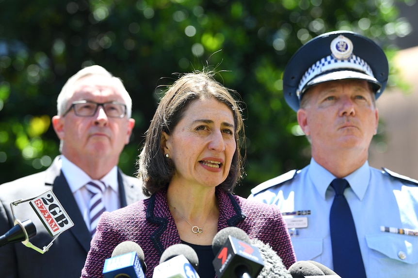 a woman talking behind a microphone with a police man and another man standing behind her