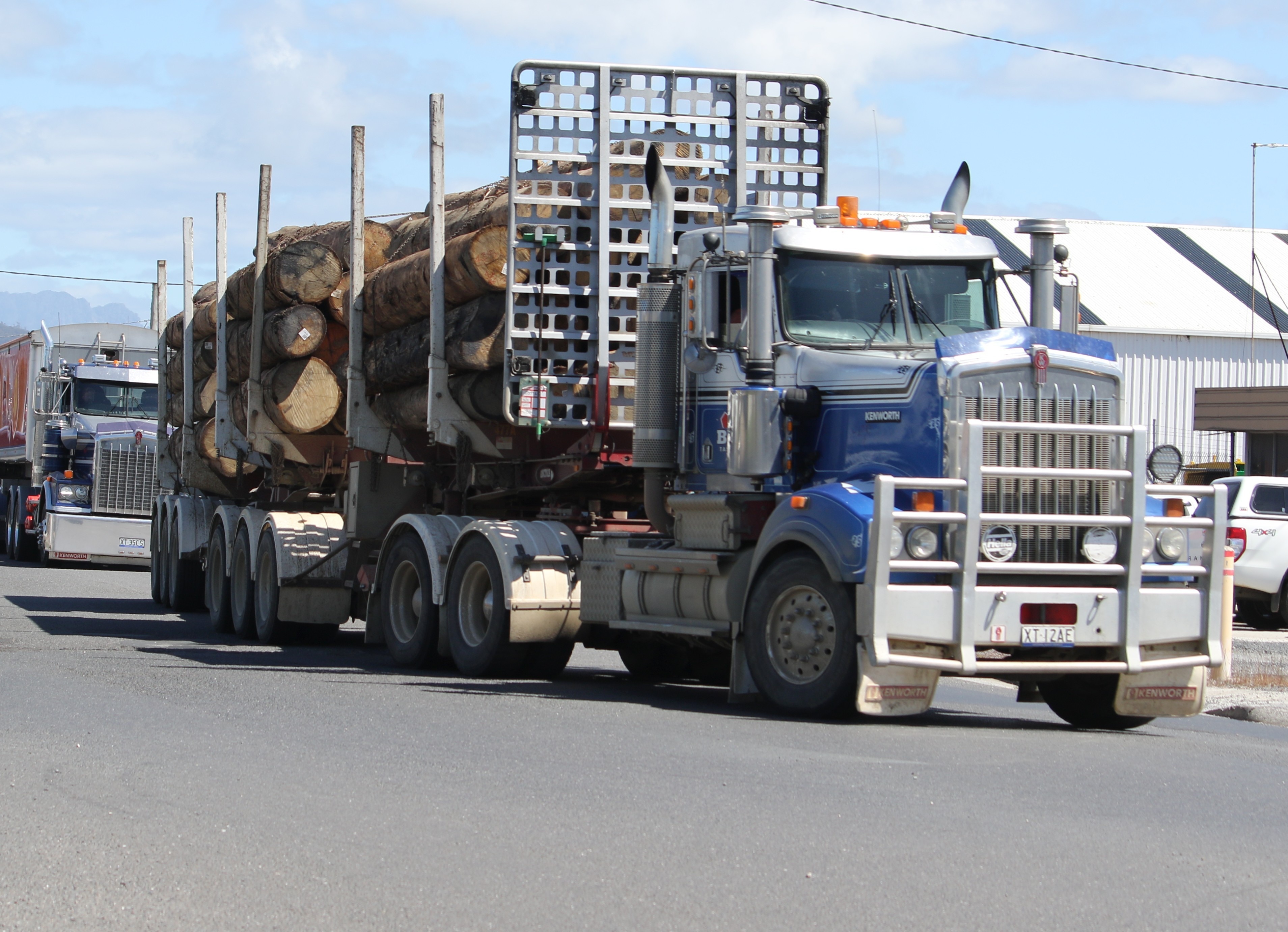 A semi-trailer loaded with logs on a road. Another truck is behind it.
