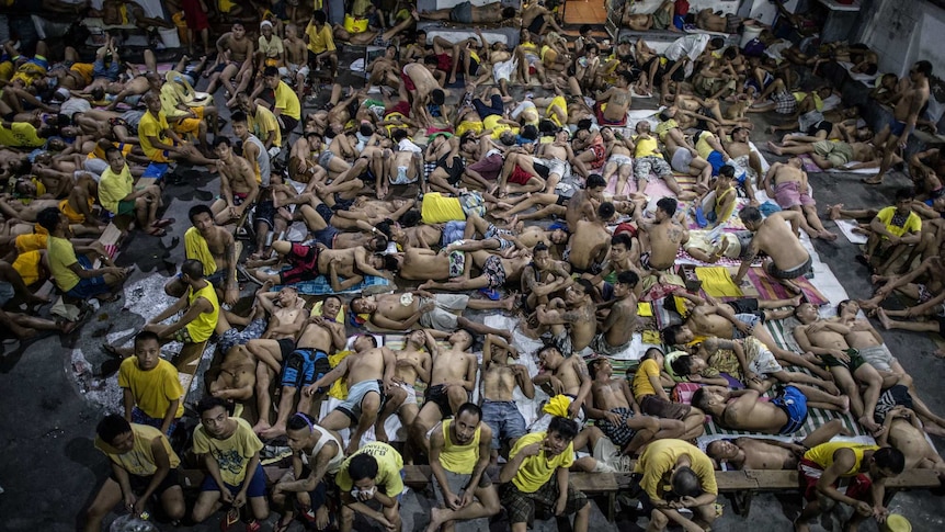 Hundreds of inmates sleep on the ground of an open basketball court