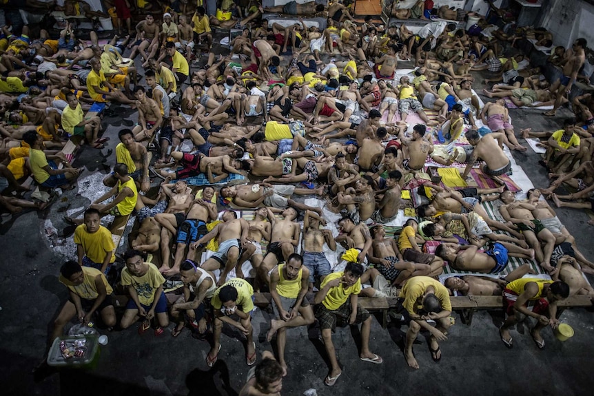 Hundreds of inmates sleep on the ground of an open basketball court