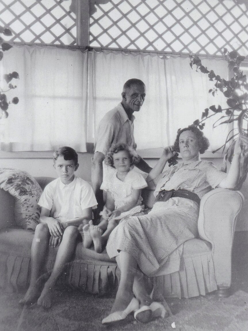 Black and white photo of family sitting on a old cane coach.