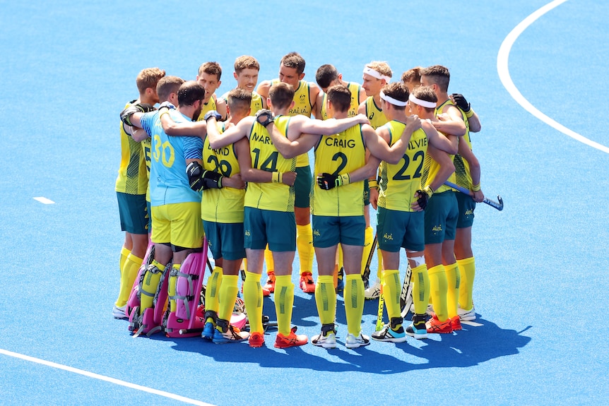 The Australian men's hockey team stand together in a huddle on the field