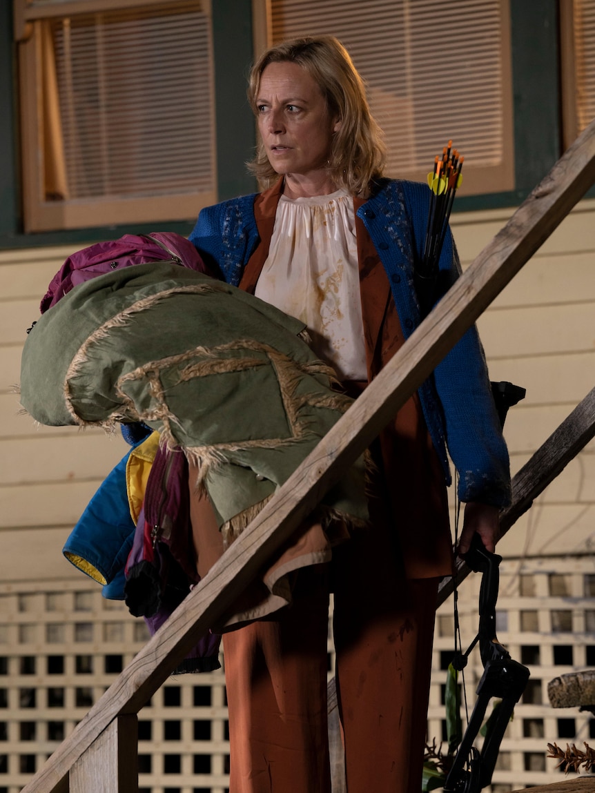 A woman holds a pile of clothes while standing on a flight of steps.