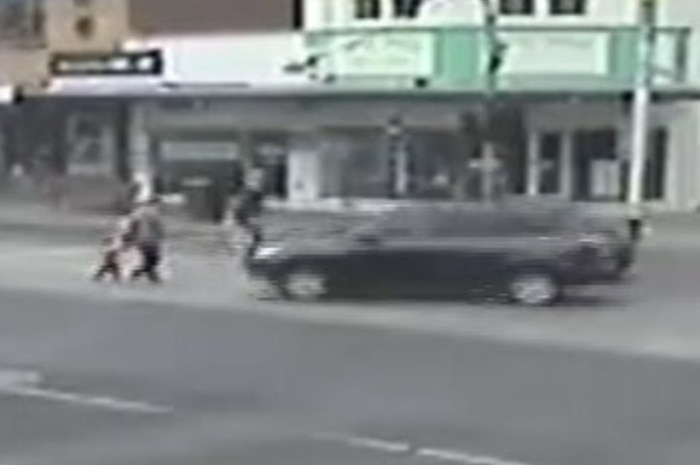 A CCTV footage still shows a black car about to hit a pair of pedestrians crossing a street.