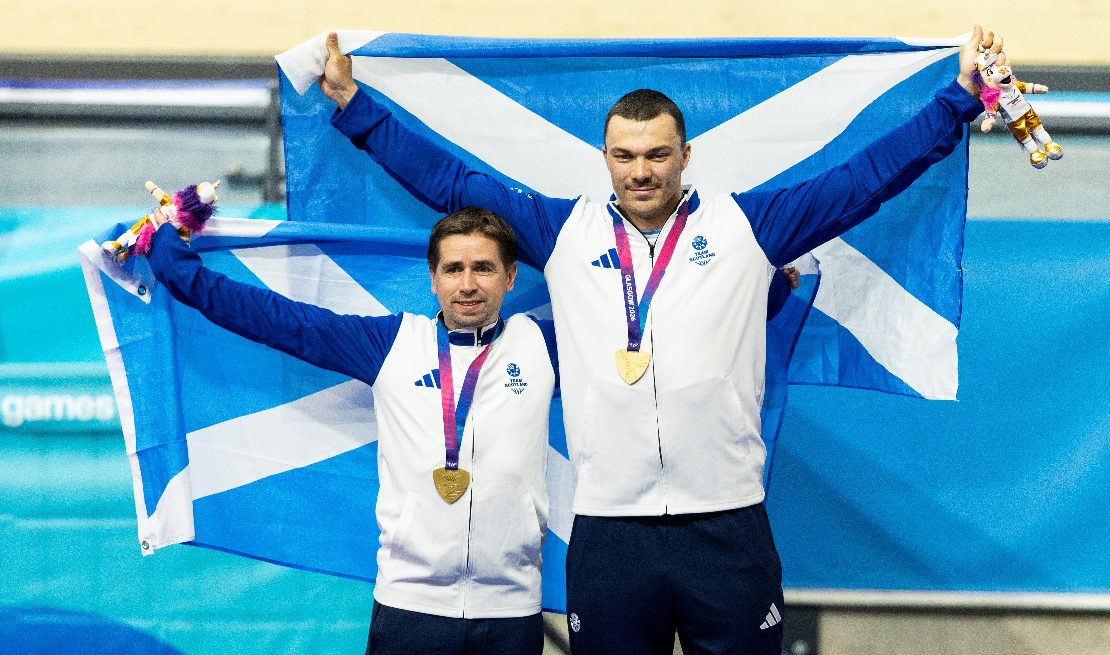 Neil Fache and Aaron Pope hold Scotland flags on the cycling podium.