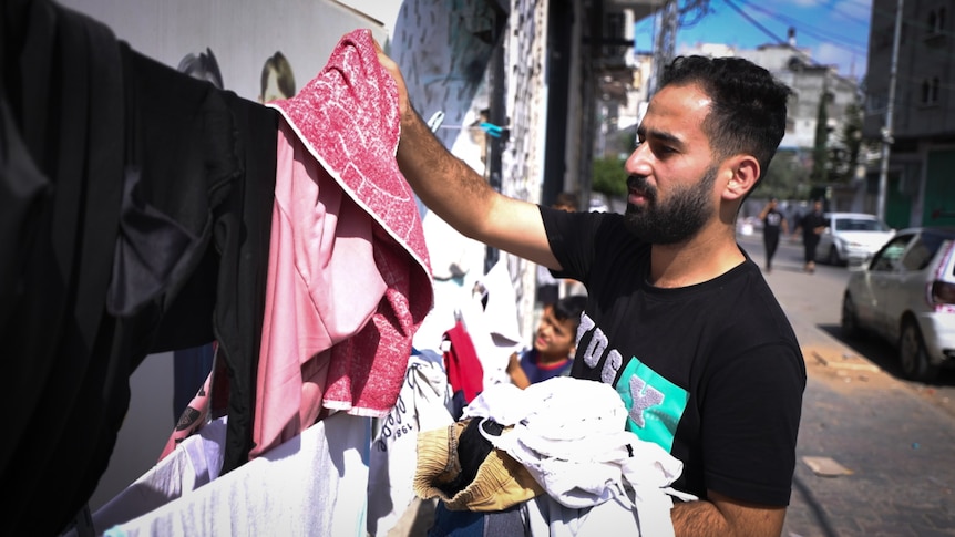 A man wearing a black Tshirt with graphic print hangs clothes on the line