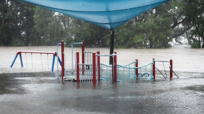 A flooded playground with a blue and beige sail above it