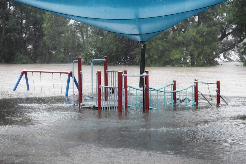 A flooded playground with a blue and beige sail above it