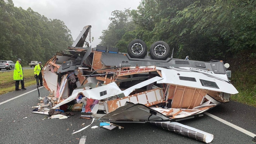 The broken shell of a caravan upside down on a wet road.