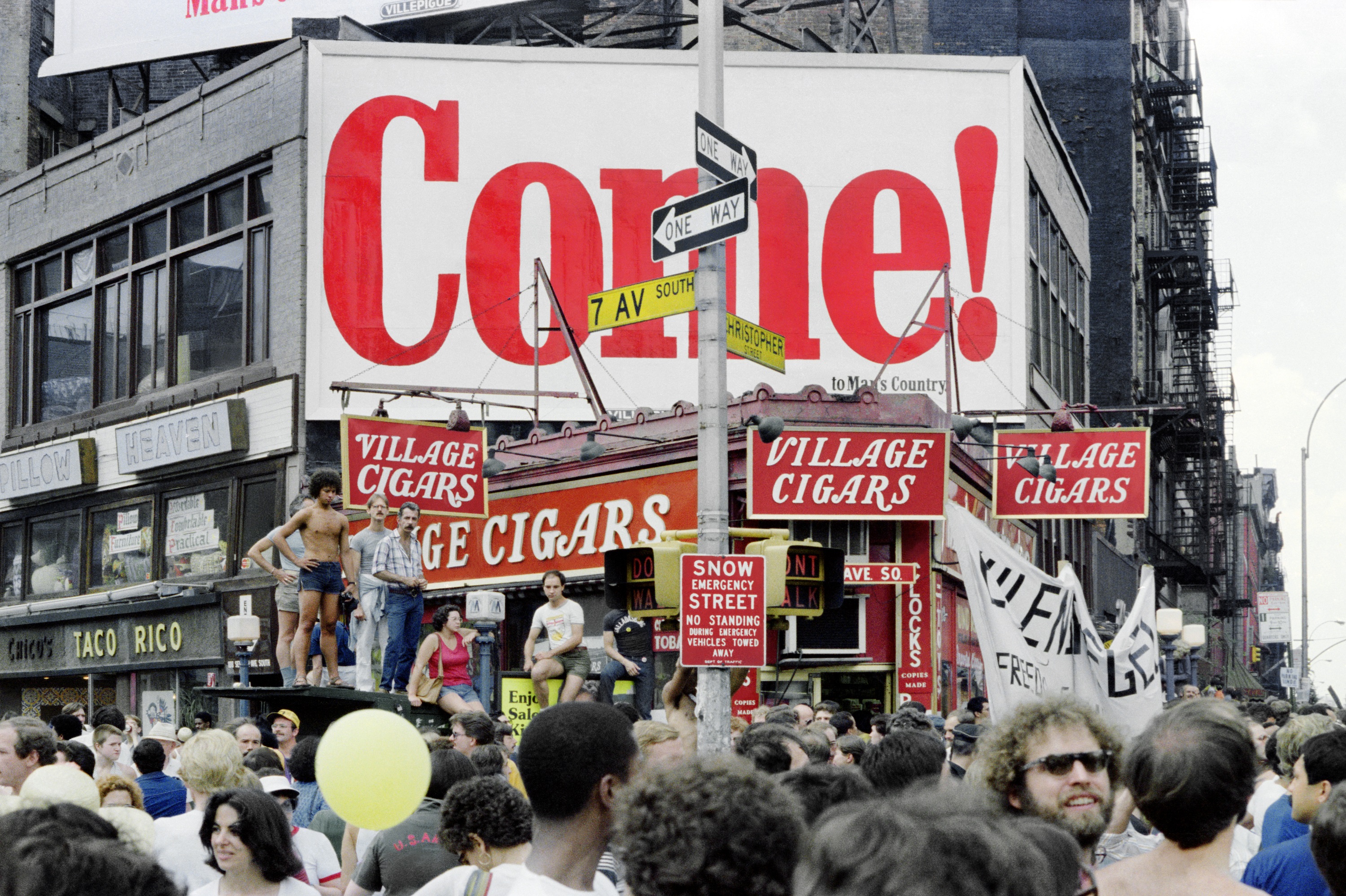 A photograph taken in 1977 of a crowded Christopher Street in New York, with a large sign reading Come! in the centre