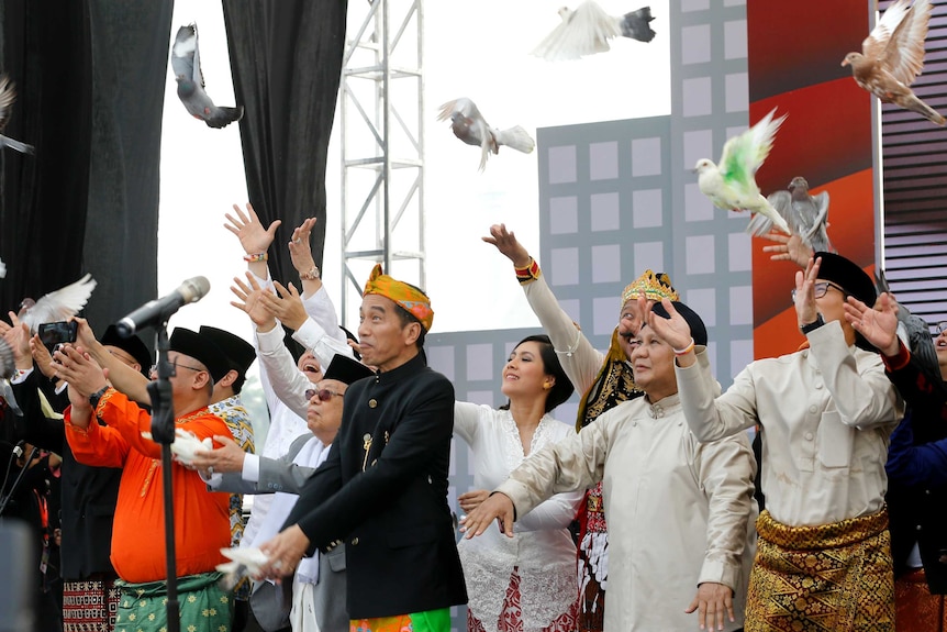 A group of men and a woman in traditional Indonesian clothing releases doves