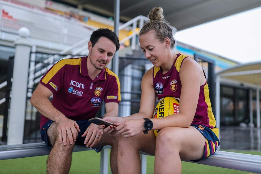 Coach Matt Green and Lions player Lauren Arnell sit together looking at an app on a mobile phone.