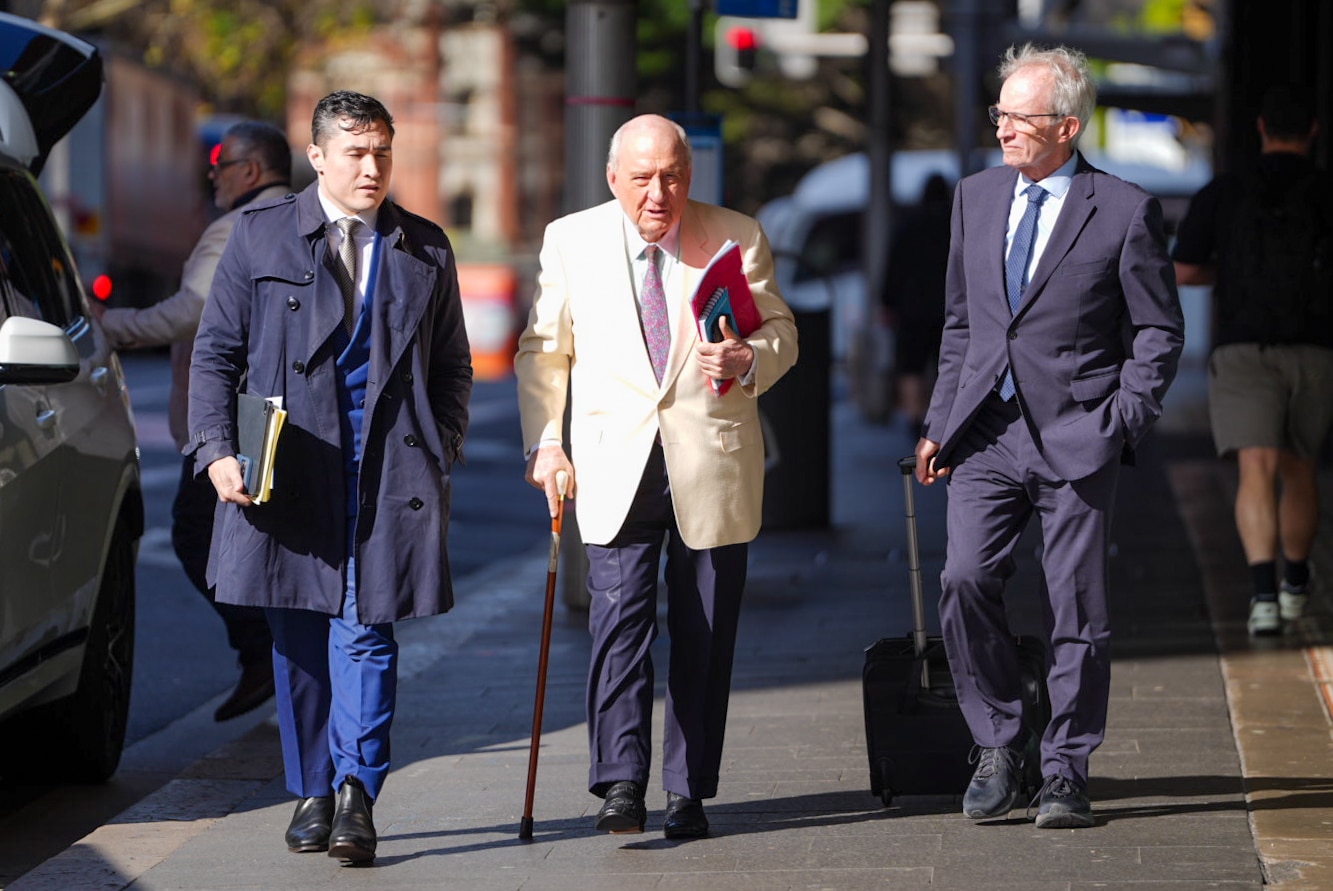 Man in a suit and light-coloured jacket with glasses walks in street