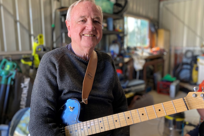 An older man with white hair holding a blue guitar