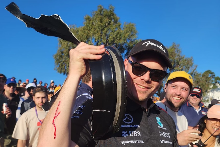 A spectator holds a piece of debris and shows a cut on his right forearm at the Australian F1 Grand Prix.