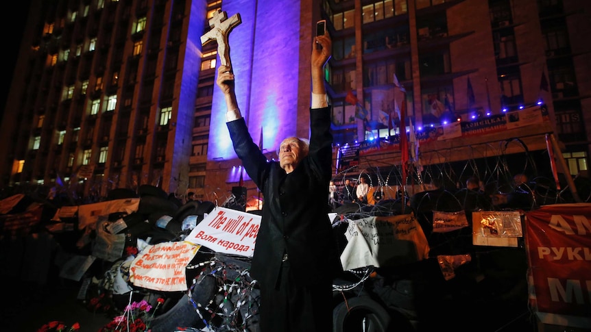 A man holds a cross and a telephone as he stands near a barricade erected by pro-Russian activists.