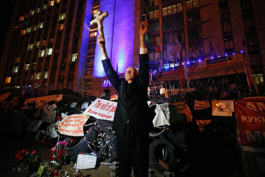 A man holds a cross and a telephone as he stands near a barricade erected by pro-Russian activists.