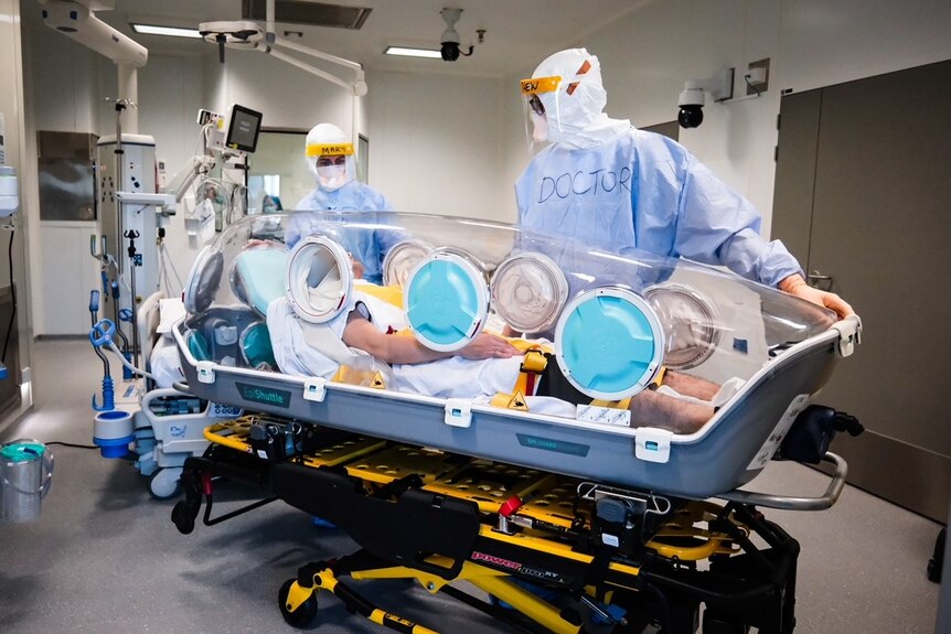Doctor in hazmat suit looks at patient in a biocontamination container