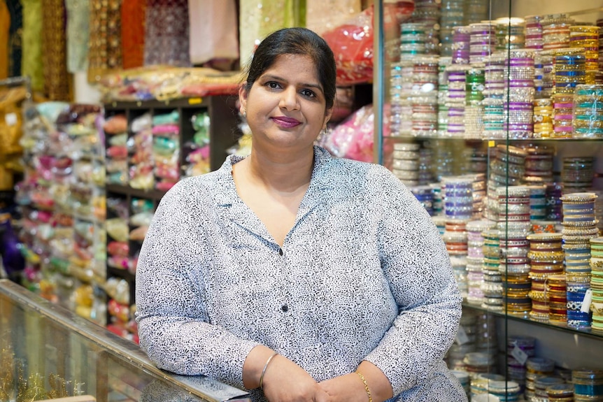 Manmeet Kaur stands inside her store, surrounded by colourful fabric and jewellery.