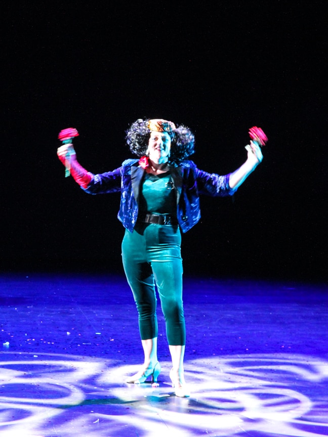 A woman stands on a stage with a blue and white floor holding up two roses.