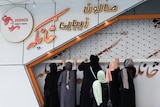 A group of women wearing burquas stand grabbing a beauty salon with orange writing 