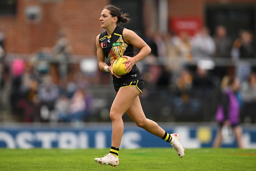 A Richmond AFLW player runs with the ball during a match.