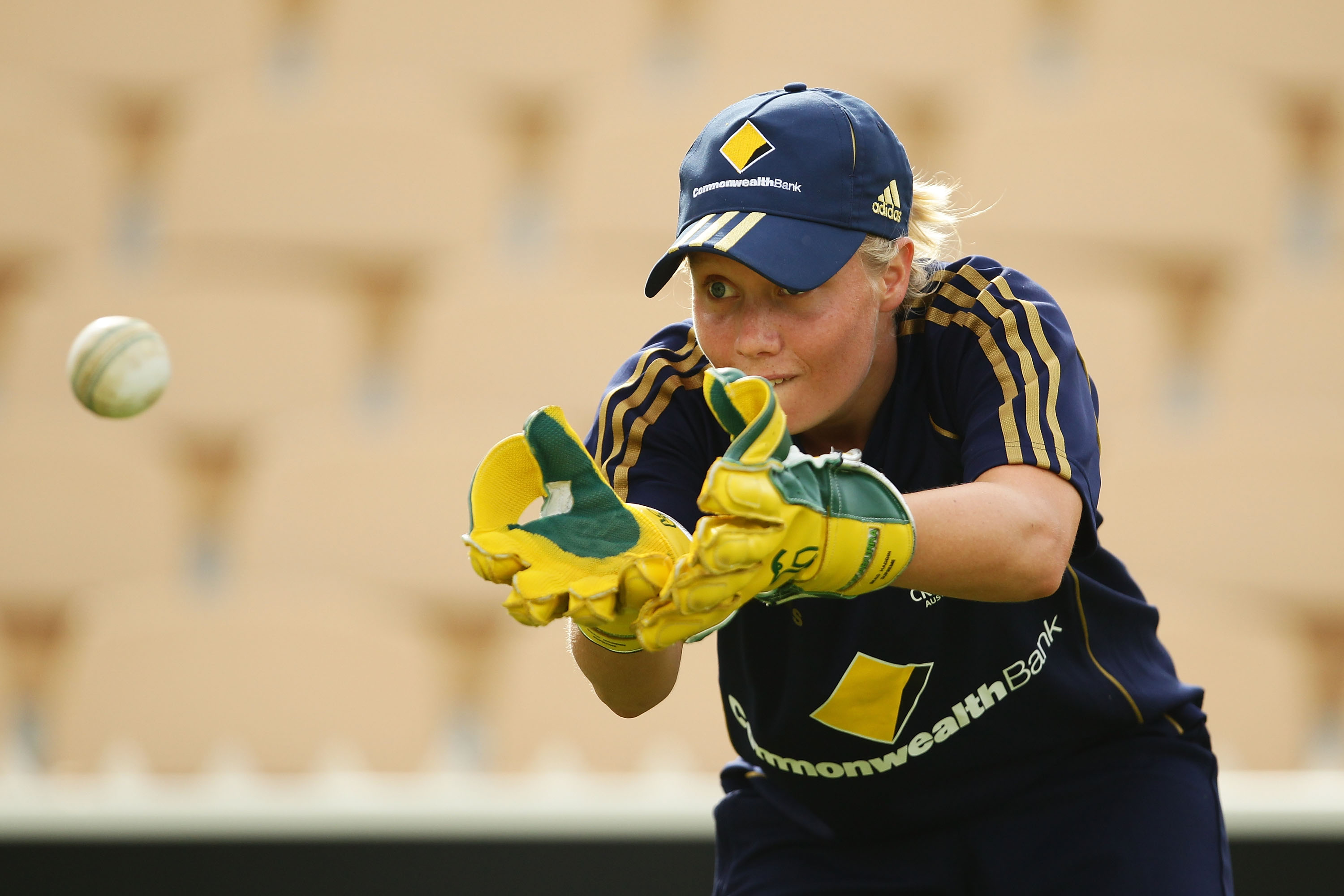 A guarda-postigo australiana, Alyssa Healy, observa uma bola branca em suas luvas durante o treinamento.