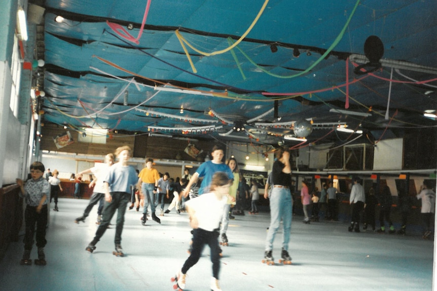 Wide shot of a roller skating rink with a crowd on it in the 1980s